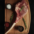 Raw steak on a wooden cutting board with rosemary and spices on a dark background