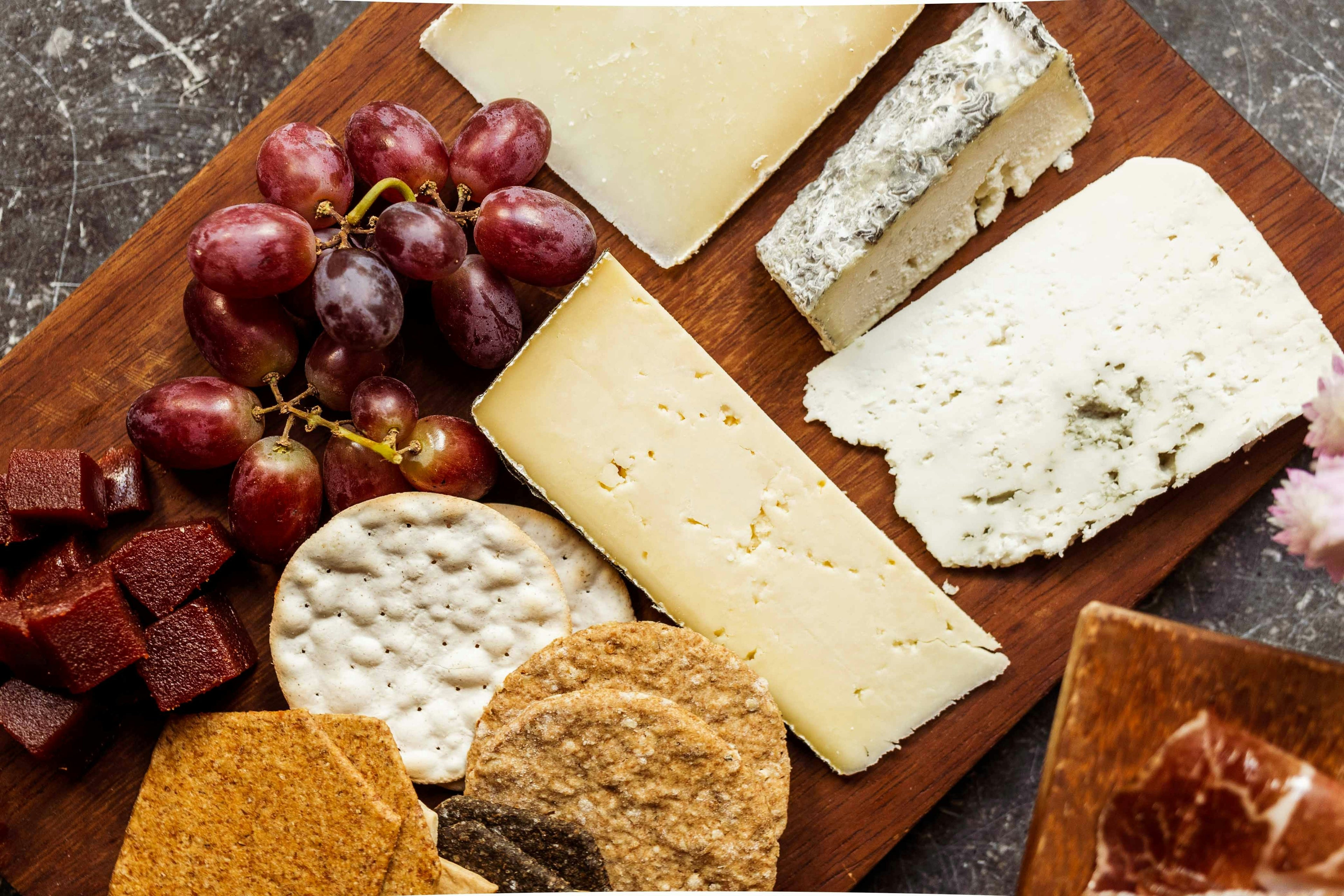 Assorted cheeses, crackers, and grapes on a wooden board.