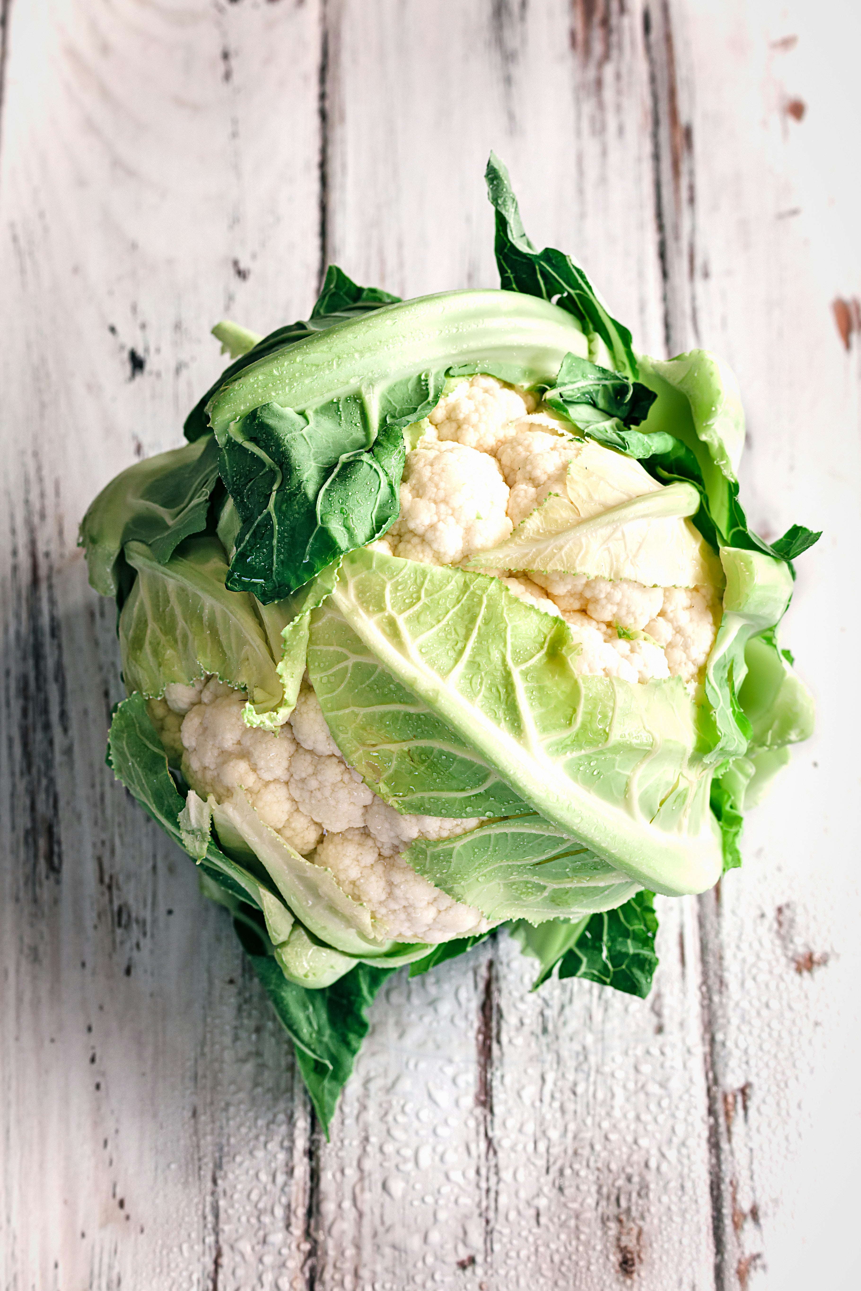 Cauliflower head with green leaves on a wooden surface